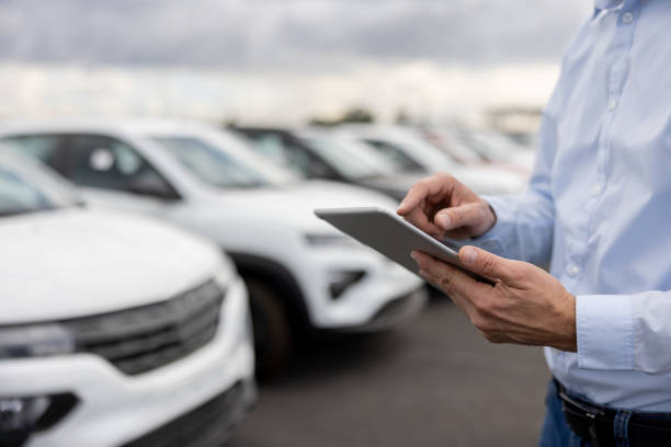 Hombre con tablet gestionando venta de coches extranjeros en un concesionario